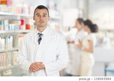 Positive male pharmacist in medical uniform posing while working in pharmacy 138943984