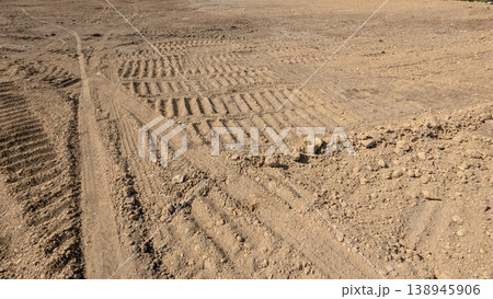 Deep tire tracks mark dry, sandy soil. Parallel grooves create a rhythmic pattern across parched ground. High angle view highlights industrial or agricultural movement on rough, dusty terrain. 138945906