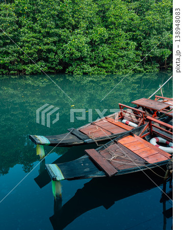 Traditional wooden boats moored in a calm green river surrounded by lush mangrove forest. Traditional wooden boats moored in a calm green river surrounded by lush mangrove forest. 138948083