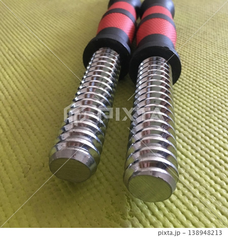 Two metal rods with textured grips placed on a green surface during a workout session in a fitness area Two metal rods with textured grips placed on a green surface during a workout session in a fitness area 138948213