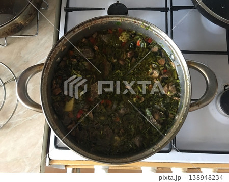 Cooking a traditional dish in a pot on a stove with fresh ingredients in a kitchen setting during the day Cooking a traditional dish in a pot on a stove with fresh ingredients in a kitchen setting during the day 138948234