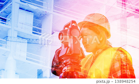 A geodesic engineer performs close-up survey work on a construction site behind a geodetic instrument. 138948254