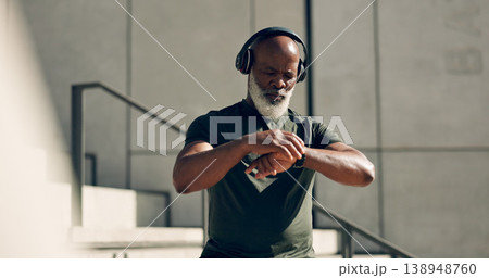 Fitness, headphones and black man on smart watch in city, workout progress and exercise results for body health. Music, senior athlete and check time on clock, heart rate and serious in town on steps 138948760