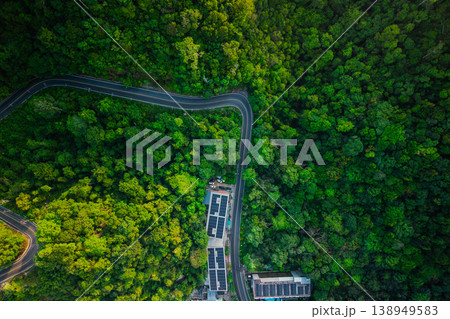 Aerial view of a winding road through lush forest with resort buildings featuring solar panels on roofs. Aerial view of a winding road through lush forest with resort buildings featuring solar panels on roofs. 138949583
