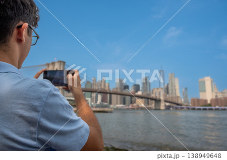 New york, usa august 15,2024. Man capturing new york city landmark brooklyn bridge and lower manhattan skyline across east river with smartphone. Travel concept 138949648