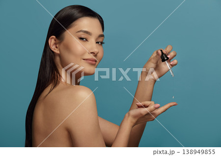Asian woman keeps cap of cosmetic vial, looks to camera. Asian woman keeps cap of cosmetic vial, looks to camera. 138949855