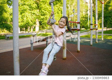 Little Girl Cheerful Smiling While Climbing Rope At Outdoor Playground Little Girl Cheerful Smiling While Climbing Rope At Outdoor Playground 138949863