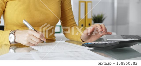 Businesswoman wearing yellow casual sweater is calculating budget and reviewing financial documents using a laptop and calculator for home finances. Audit and taxes in business Businesswoman wearing yellow casual sweater is calculating budget and reviewing financial documents using a laptop and calculator for home finances. Audit and taxes in business 138950582