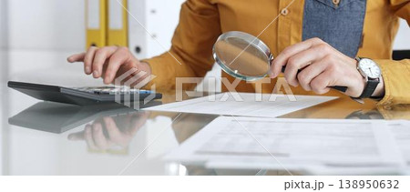 Accountant analyzing financial data with magnifying glass, calculating expenses, and auditing documents at office desk. Audit and taxes in business Accountant analyzing financial data with magnifying glass, calculating expenses, and auditing documents at office desk. Audit and taxes in business 138950632