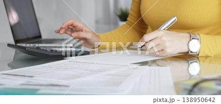 Businesswoman wearing yellow casual sweater is calculating budget and reviewing financial documents using a laptop and calculator for home finances. Audit and taxes in business Businesswoman wearing yellow casual sweater is calculating budget and reviewing financial documents using a laptop and calculator for home finances. Audit and taxes in business 138950642