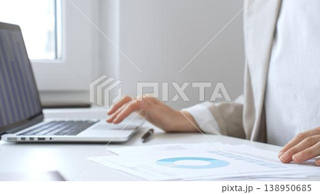 Businesswoman analyzing financial reports, reviewing charts on laptop and paper documents while seated at desk in office workspace. Business people concept 138950685
