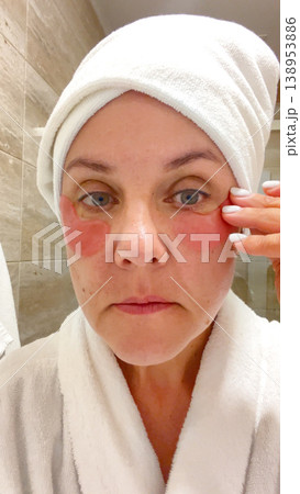A middle-aged woman applies cosmetic patches to the skin under the eyes.  138953886