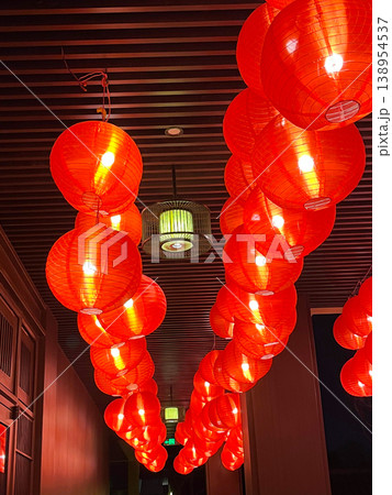 Glowing round red paper lanterns hanging in rows from a dark slatted wooden ceiling for Asian cultural events and interior design decoration themes 138954537