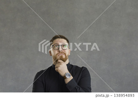 Puzzled and confused man with a pensive expression looking up on a gray concrete background. Puzzled and confused man with a pensive expression looking up on a gray concrete background. 138954893