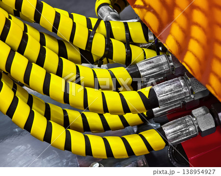 Hoses with yellow and black stripes connect to machinery in an industrial setting during daylight hours Hoses with yellow and black stripes connect to machinery in an industrial setting during daylight hours 138954927