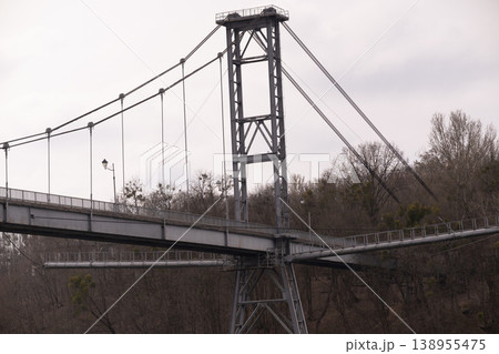 Large Gray Metal Suspension Bridge Structure Against Overcast Sky and Winter Trees 138955475
