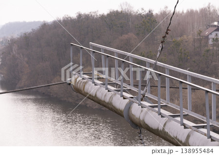 Industrial Suspension Bridge Structure with Metal Railing Over River in Misty Landscape 138955484