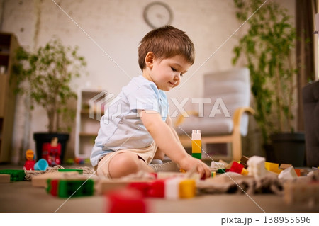 Little boy building structure with plastic blocks sitting on floor in modern living room 138955696
