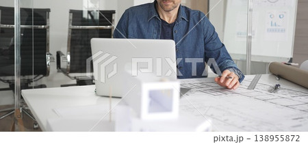 Architect working on new design development in modern office, planning construction project, drawing blueprints, conceptualizing architectural model with laptop Architect working on new design development in modern office, planning construction project, drawing blueprints, conceptualizing architectural model with laptop 138955872
