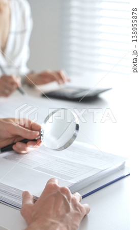Team of accountants are working together, using a magnifying glass and a calculator, to audit financial reports in office. Audit and taxes concept Team of accountants are working together, using a magnifying glass and a calculator, to audit financial reports in office. Audit and taxes concept 138955878