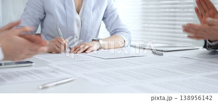 Businesswoman signing important contract documents at a meeting. Confirming agreement and partnership details while colleagues show support 138956142