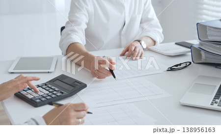 Two accountants collaborating in a well lit office, analyzing financial data and preparing reports with calculators and pens. Audit and taxes in business Two accountants collaborating in a well lit office, analyzing financial data and preparing reports with calculators and pens. Audit and taxes in business 138956163