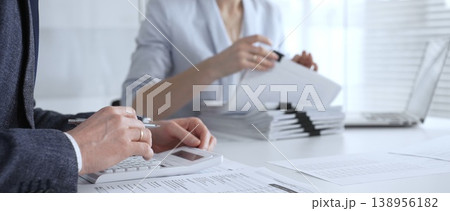 Business professionals working on financial reports, calculating taxes and managing paperwork at an office desk, collaborating on accounting tasks and corporate documentation. Audit and taxes 138956182