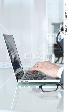 Businessman in a modern office intently typing on a laptop, deeply focused and analyzing data to develop solutions and strategies for projects and corporate challenges Businessman in a modern office intently typing on a laptop, deeply focused and analyzing data to develop solutions and strategies for projects and corporate challenges 138956227