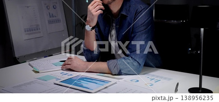 Man analyzing financial charts and business data on tablet in late night office, working overtime on a new project, thinking about solution and strategy Man analyzing financial charts and business data on tablet in late night office, working overtime on a new project, thinking about solution and strategy 138956235