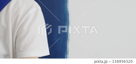 Painter applying blue paint with roller on white wall, showing precise technique and transforming interior space with smooth, even strokes Painter applying blue paint with roller on white wall, showing precise technique and transforming interior space with smooth, even strokes 138956320