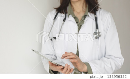 Unknown professional woman doctor, wearing white coat over a green blouse and a stethoscope, is using a digital tablet, suggesting innovative healthcare practices in medicine. Health care concept 138956322