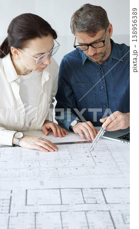 Architects collaborating on blueprint plans, discussing engineering details and project designs, planning construction development with a laptop in a modern office environment 138956389