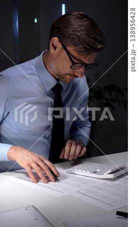 Accountant working late night in office, calculating finance data and economy statistics in a blue shirt with a tie. Audit and taxes in business 138956428