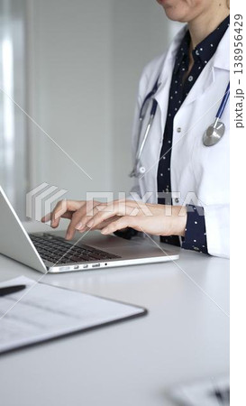 Professional doctor reviewing electronic medical records and typing information on laptop during remote consultation. Medicine, healthcare and science concept 138956429