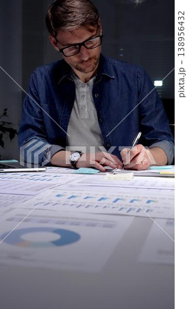 Professional man in glasses working late at night, analyzing financial data on a digital tablet, managing business reports, and extending productivity in a dark office environment Professional man in glasses working late at night, analyzing financial data on a digital tablet, managing business reports, and extending productivity in a dark office environment 138956432