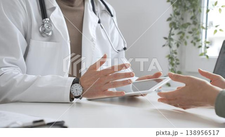 Male doctor in lab coat and stethoscope listening to patient while using tablet in modern medical office. Medicine and health care concept Male doctor in lab coat and stethoscope listening to patient while using tablet in modern medical office. Medicine and health care concept 138956517