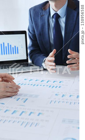 Businessman sitting at the table and pointing into financial charts while discussing financial data, market trends with colleagues during a corporate meeting in office. Business people concept Businessman sitting at the table and pointing into financial charts while discussing financial data, market trends with colleagues during a corporate meeting in office. Business people concept 138956588