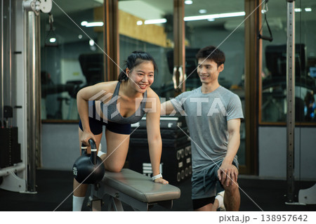 A woman is performing a kettlebell row on a bench while her trainer closely checks her form A woman is performing a kettlebell row on a bench while her trainer closely checks her form 138957642