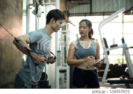 Asian men exercise chest workout on cable chest press personal trainer is reviewing progress Asian men exercise chest workout on cable chest press personal trainer is reviewing progress 138957672