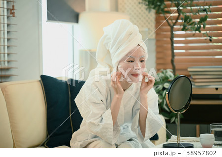 Young woman in bathrobe adjusts facial sheet mask at home 138957802