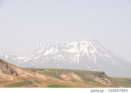 Mount Hasan Volcano Cappadocia Landscape. Majestic snow-capped Mount Hasan peaks over green spring fields in Cappadocia, Turkey. Mount Hasan Volcano Cappadocia Landscape. Majestic snow-capped Mount Hasan peaks over green spring fields in Cappadocia, Turkey. 138957804