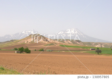 Mount Hasan Volcano Cappadocia Landscape. Majestic snow-capped Mount Hasan peaks over green spring fields in Cappadocia, Turkey. Mount Hasan Volcano Cappadocia Landscape. Majestic snow-capped Mount Hasan peaks over green spring fields in Cappadocia, Turkey. 138957805