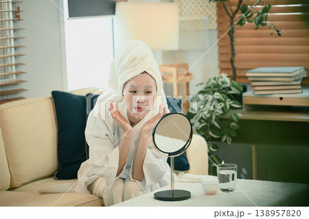 Young woman in bathrobe adjusts facial sheet mask at home 138957820