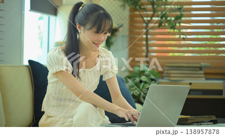 Young woman smiling while working on laptop indoors Young woman smiling while working on laptop indoors 138957878