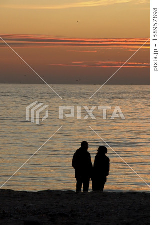 Silhouette of Couple on Beach at Sunset. A peaceful scene of a couple enjoying a golden sunset by the calm sea, captured in silhouette on a sandy shore. Silhouette of Couple on Beach at Sunset. A peaceful scene of a couple enjoying a golden sunset by the calm sea, captured in silhouette on a sandy shore. 138957898