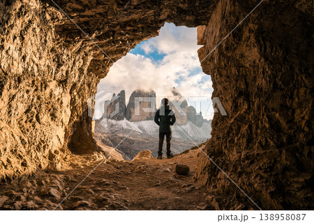 Male tourist standing at front of rock cave of Grotta delle Tre Cime with mountain peak in Dolomites, Italy Male tourist standing at front of rock cave of Grotta delle Tre Cime with mountain peak in Dolomites, Italy 138958087