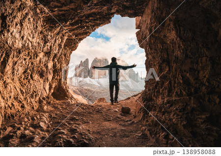 Male tourist standing at front of rock cave of Grotta delle Tre Cime with mountain peak in Dolomites Male tourist standing at front of rock cave of Grotta delle Tre Cime with mountain peak in Dolomites 138958088