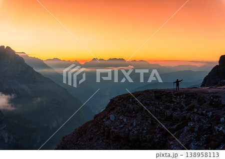 Hiker standing on mountain ridge at sunrise with dramatic alpine landscape in Dolomites Hiker standing on mountain ridge at sunrise with dramatic alpine landscape in Dolomites 138958113