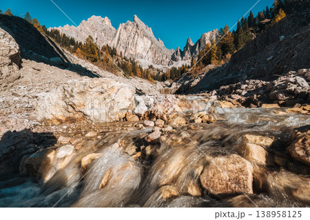 Alpine landscape of Dolomites rugged mountain and water flows in autumn larch forest 138958125