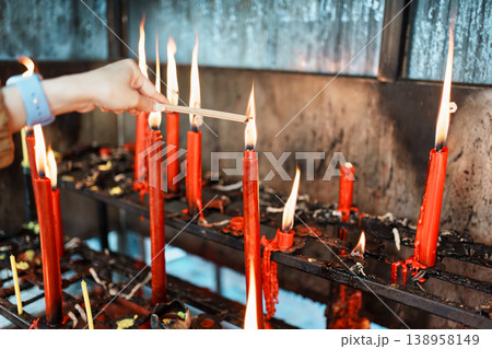 Hand of woman lighting red candles with incense sticks in chinese temple 138958149